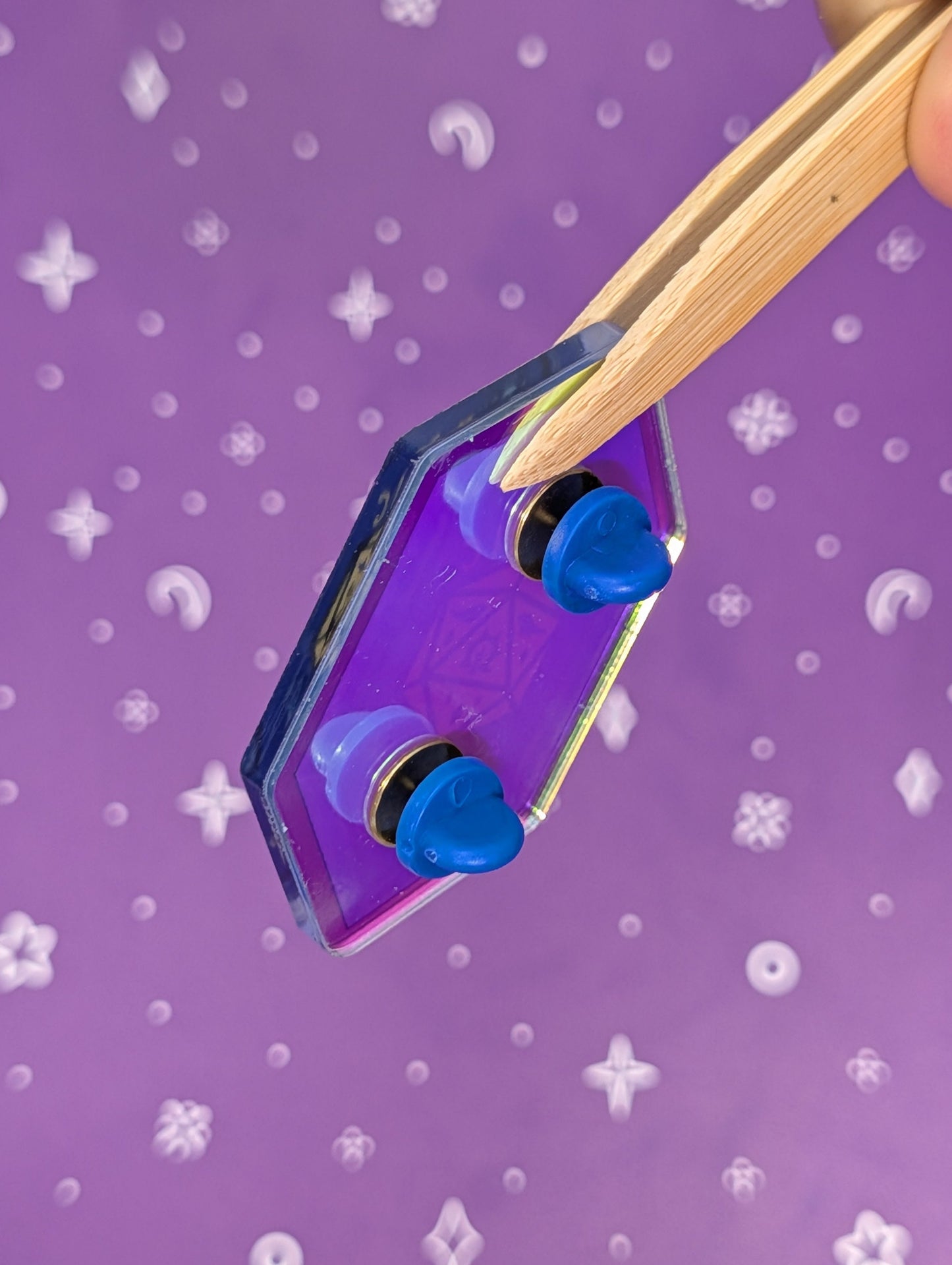 Purple crystal with blue stones held by tweezers against a purple patterned background
