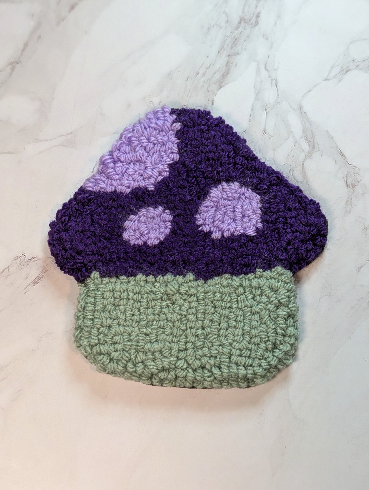 punch needle mushroom with purple cap and green body on a white marble surface