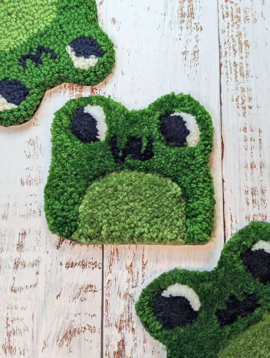 punch needle and rug tufted frog mug rugs on a wood surface