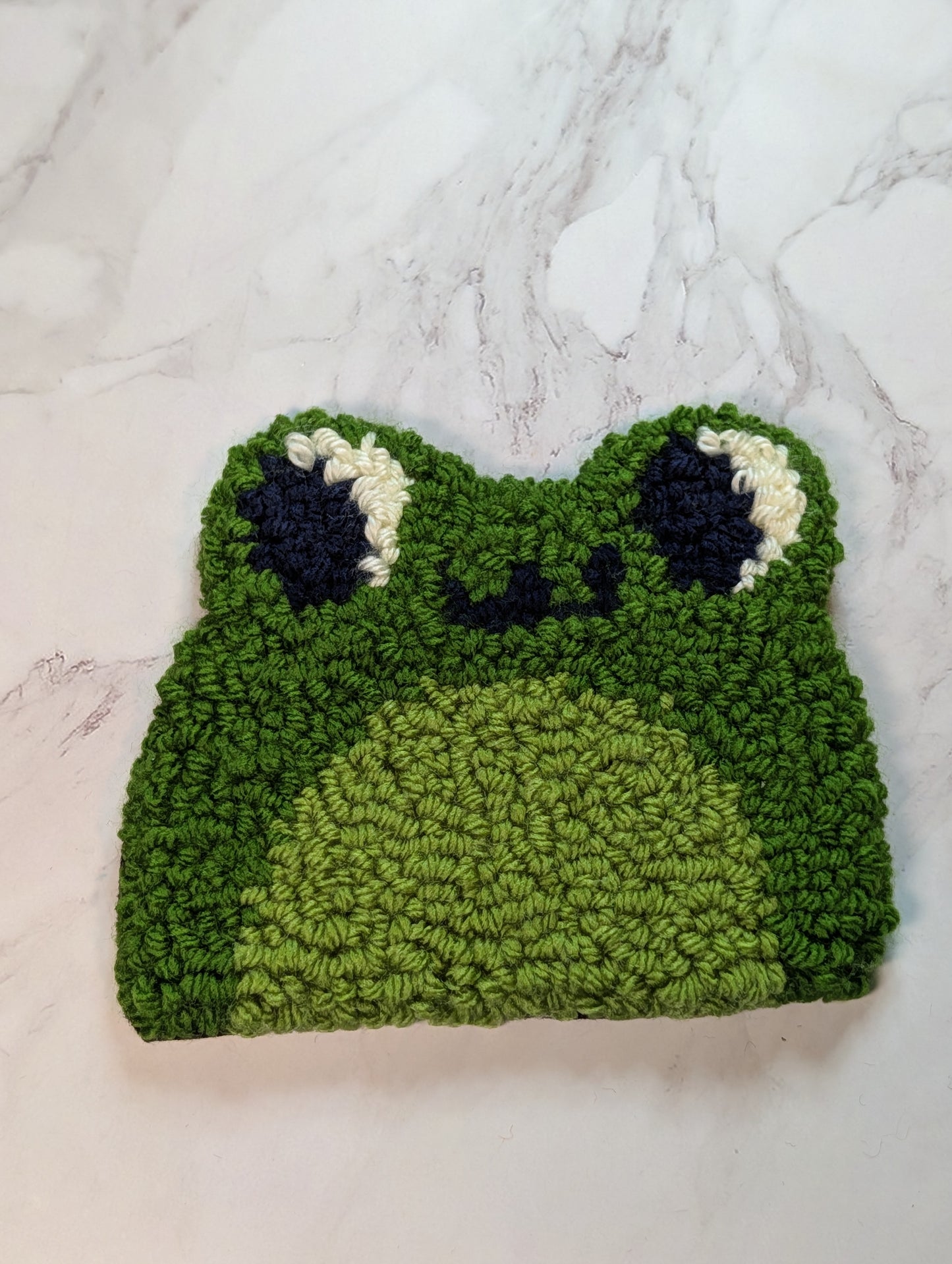 punch needle frog mug rug on a marble surface