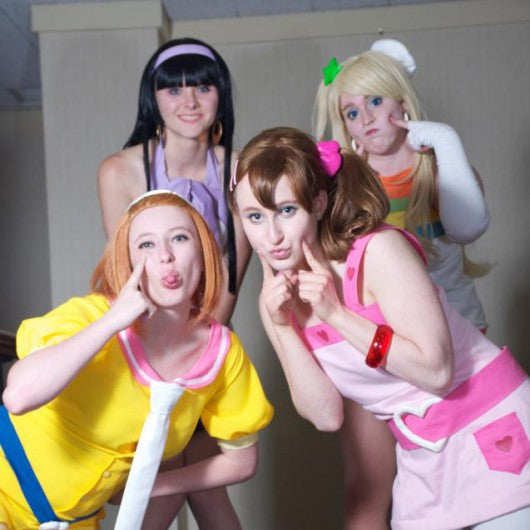 Four women posing together in colorful anime cosplay outfits, making playful faces indoors.