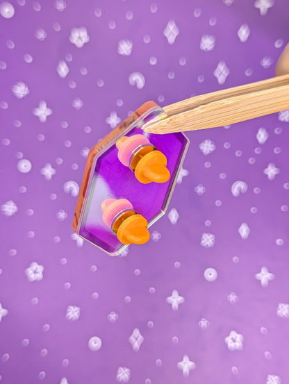 hexagon gem pin back with orange rubber backs on a purple background with white stars
