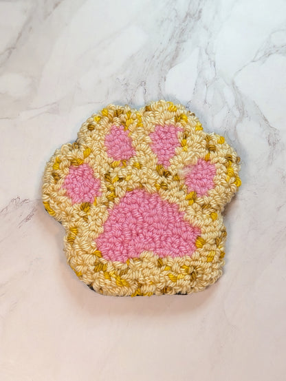 punch needle mug rug paw print in tan multi color on a white marble surface