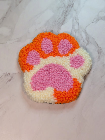 punch needle paw-shaped mug rug with orange and pink colors on a marble background