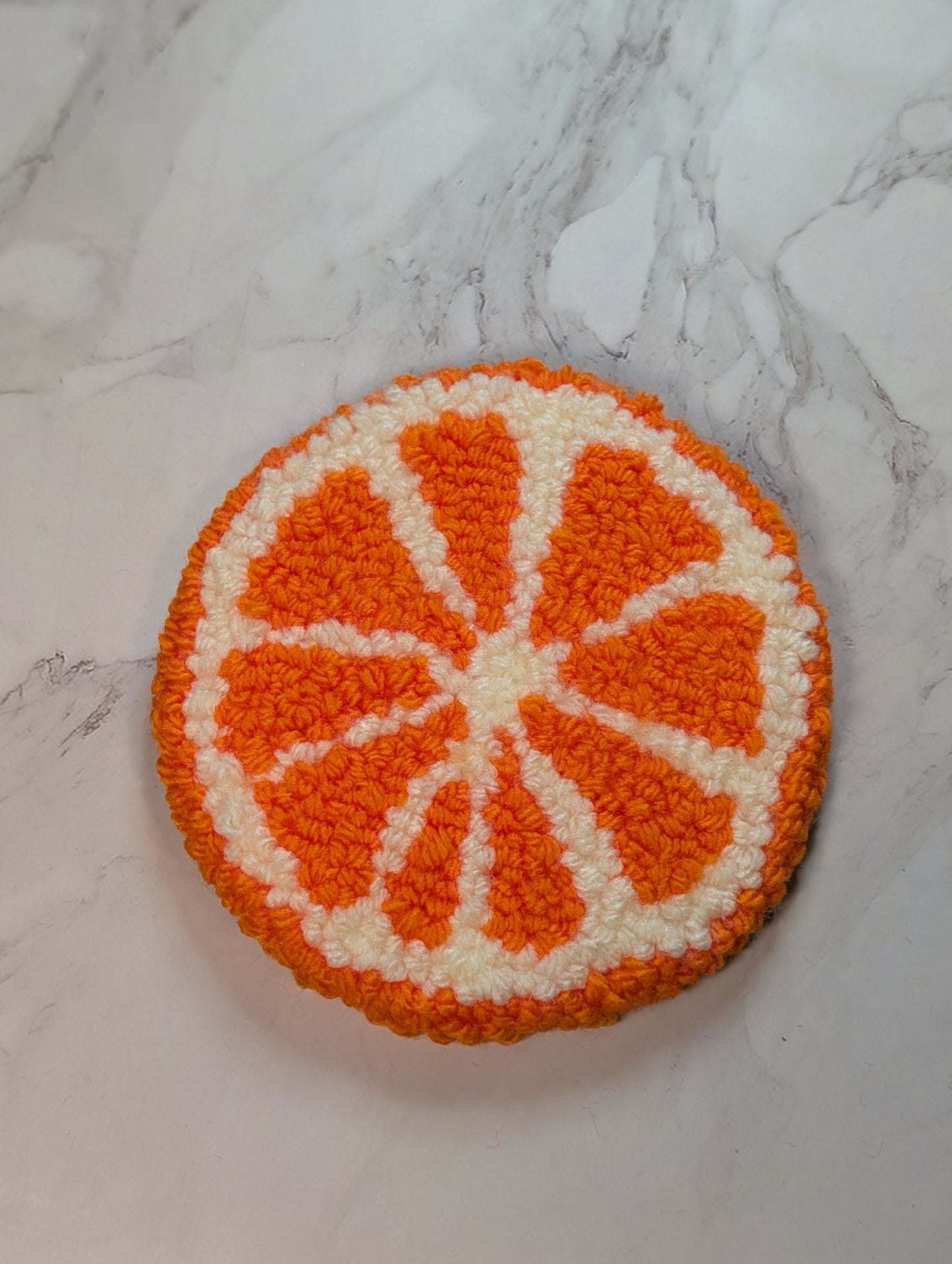 punch needle orange slice coaster on a marble surface
