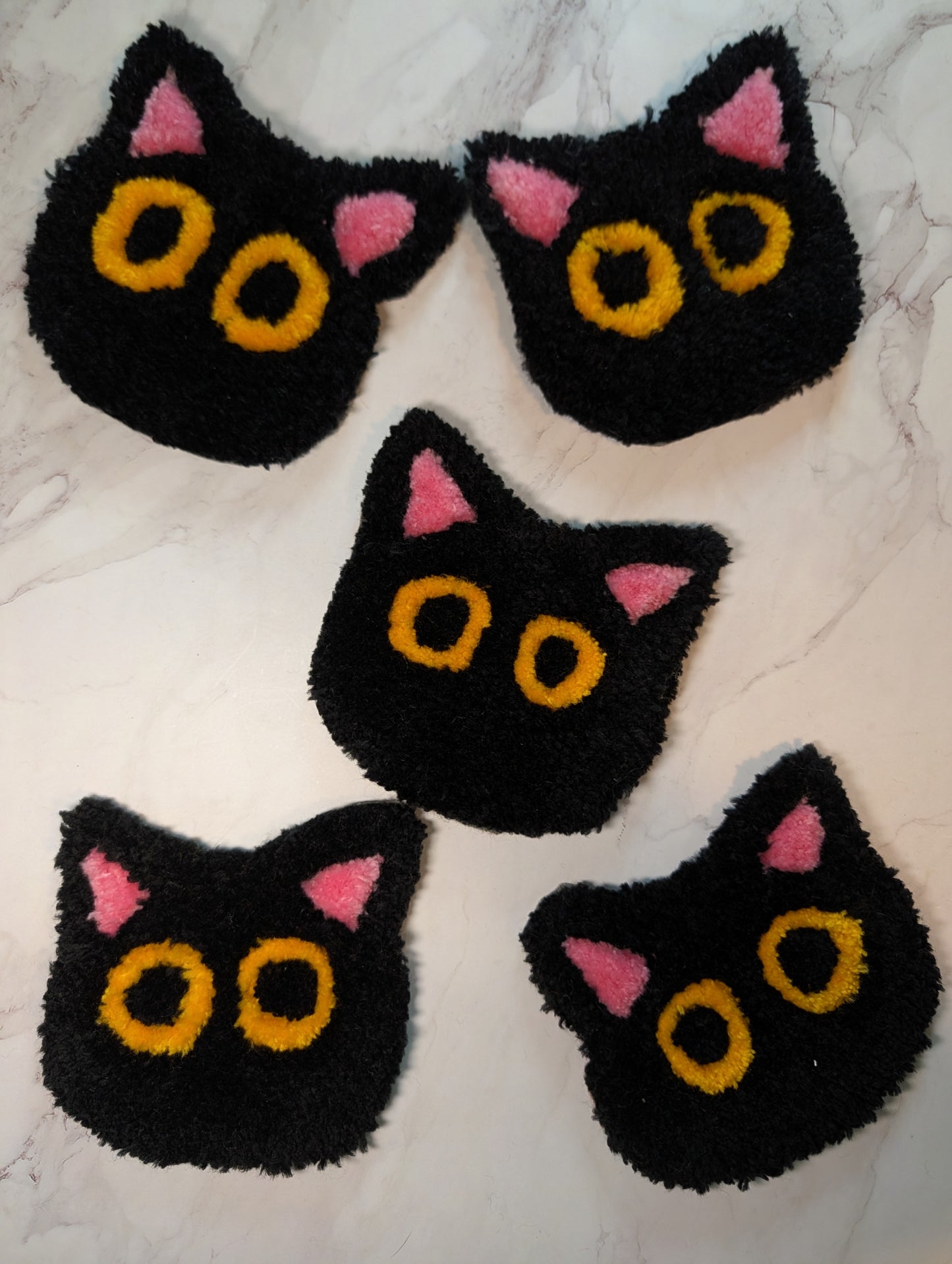 five Black cat-shaped tufted mug rug  with pink ears and yellow eyes on a white background