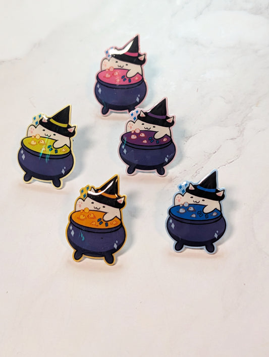 Set of five cartoon-style pins with cats in witch hats and cauldrons on a white background